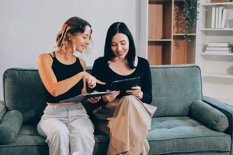Two young female students using a laptop while sitting on a sofa at home. S.. Stock Photos