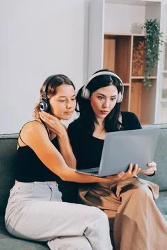 Two young female students using a laptop while sitting on a sofa at home. S.. Stock Photos