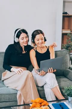 Two young female students using a laptop while sitting on a sofa at home. S.. Stock Photos