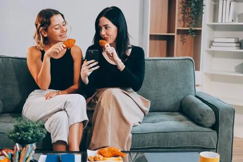 Two young female students using a laptop while sitting on a sofa at home. S.. Stock Photos