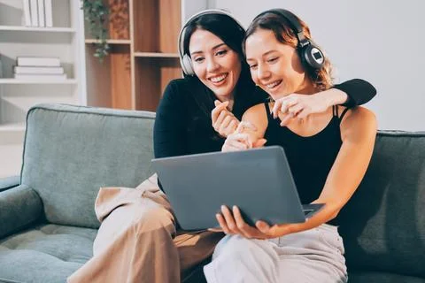 Two young female students using a laptop while sitting on a sofa at home. S.. Stock Photos