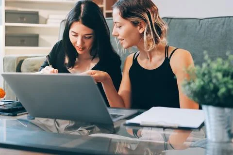 Two young female students using a laptop while sitting on a sofa at home. S.. Stock Photos
