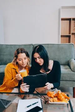 Two young female students using a laptop while sitting on a sofa at home. S.. Stock Photos