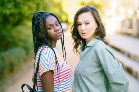 Two young friends looking at camera together on the street. Multiethnic women. Fotos de archivo