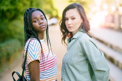 Two young friends looking at camera together on the street. Multiethnic women. Stock Photos