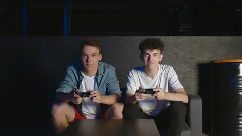 Two young friends playing action video game in the living room sitting on the Video stock 136331684