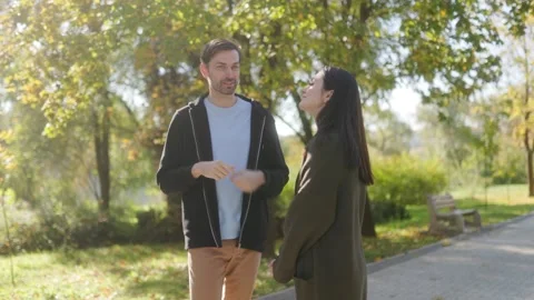Two young friends talking in a park, enjoying a relaxed autumn afternoon. Stock Footage 303988344