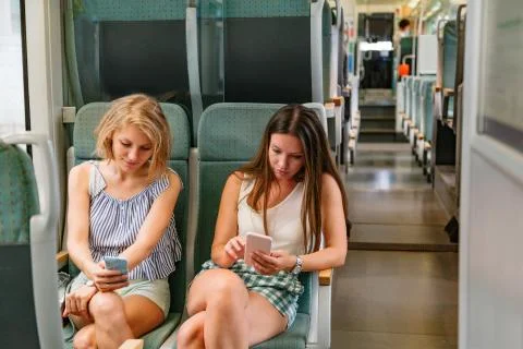 Two young girlfriends using smart phone in a train Stock Photos