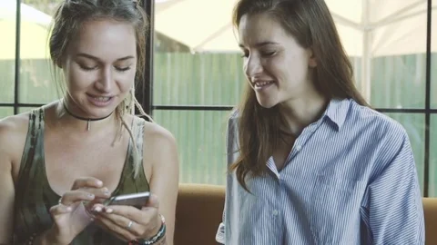 Two young girlfriends using smartphone and talking in cafe Stock Footage 73096076