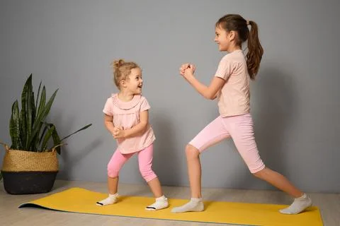 Two young girls are having fun while exercising together on a yellow yoga m.. Stock Photos
