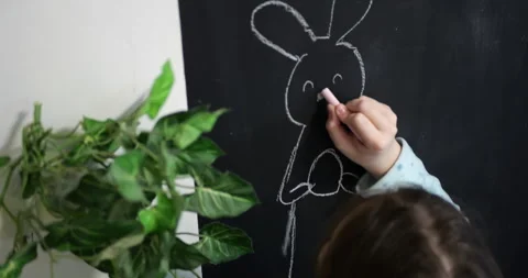 Two young girls drawing Easter decorations with chalk on black slate board Stock Footage 319787699