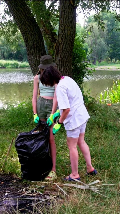 Two young girls fill trash bags near the riverbank Stock Footage 340577195