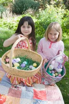 Two young girls holding Easter baskets and kneeling on patchwork quilt Stock Photos