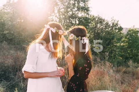 Two young girls hug during sunset in the field with wine glasses friendship c Stock Photos