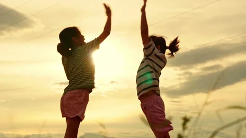 Two young girls jumping and giving high five at sunset Vídeo Stock 337748383