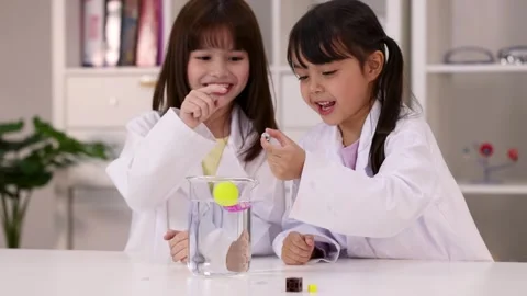 Two Young Girls in Lab Coats Conducting Science Experiment with Beaker Stock Footage 346367047