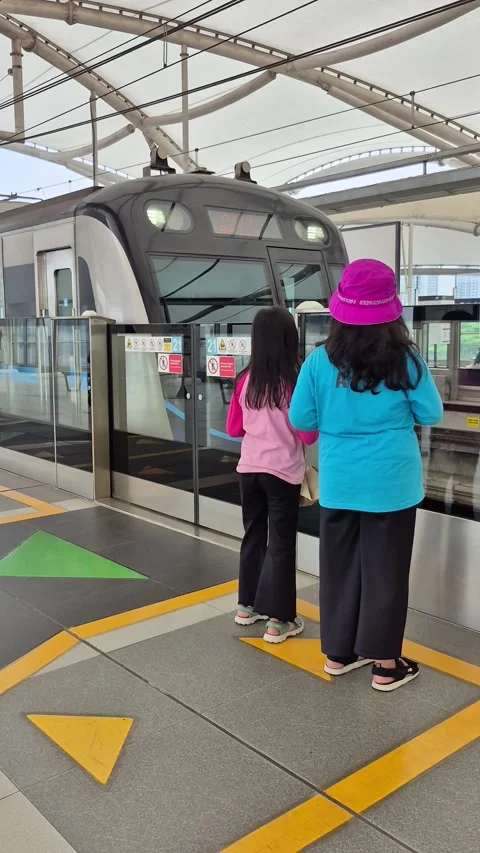 Two young girls seen from behind waiting for an approaching MRT train Stock Footage 339307045