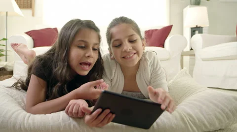 Two young girls sit on the floor and read a tablet together Stockbeeldmateriaal 34014646