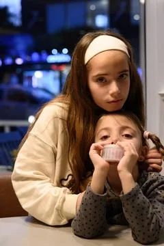 Two young girls sit at a table, one holding a cupcake Stock Photos