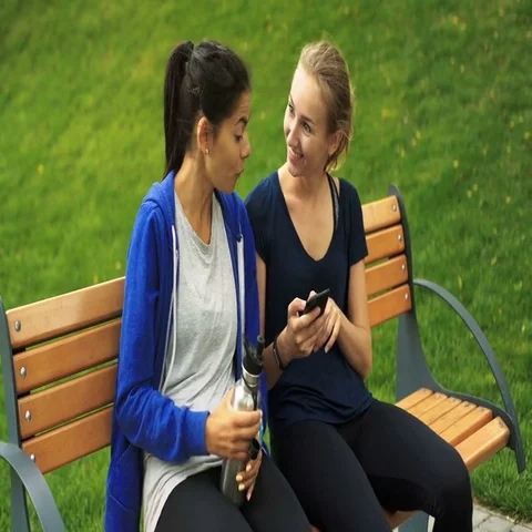 Two young girls sitting on a bench, one girl holding smartphone, other one Stock Footage 69522708
