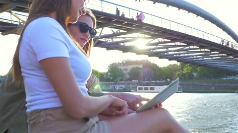 Two young girls sitting next to the river and using tablet pc. Stock Footage 65397802