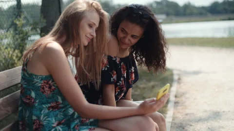 Two young girls using mobile phone while sitting on a bench. Stock Footage 93834622