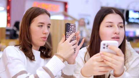 Two young girls using mobile phones while sitting at the cafe indoors mall. Two Stock Footage 266816953