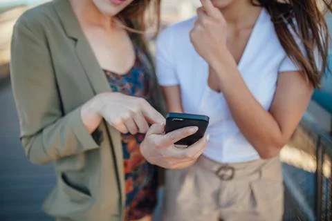 Two young girls using mobile phone. they areon the bridge. Close up. Stock Photos