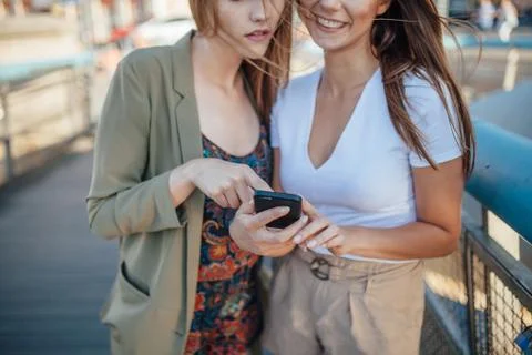Two young girls using mobile phone. they areon the bridge. Close up. Stock Photos
