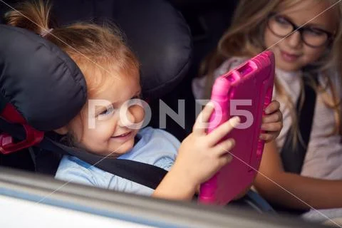 Two Young Girls Watching Digital Tablet In Back Seat On Car Journey Stock Photos