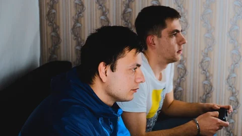 Two young guys are sitting on the couch in front of the TV and playing a game Stock Footage 129688385