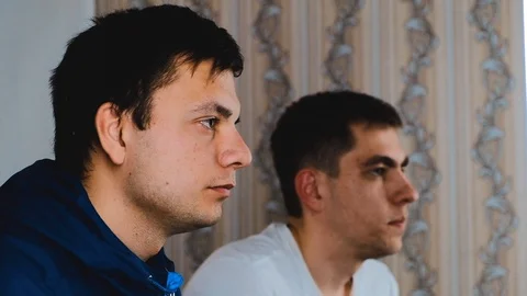 Two young guys are sitting on the couch in front of the TV and playing a game Stock Footage 129688459