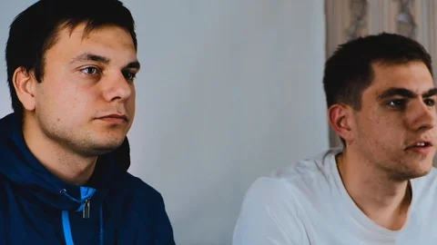 Two young guys are sitting on the couch in front of the TV and playing a game Stock Footage 129688468