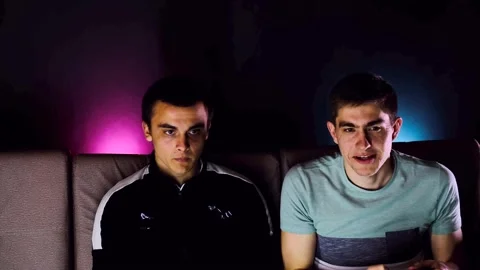 Two young guys are sitting on the couch in front of the TV and playing a game co Stock Footage 131173663