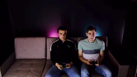 Two young guys are sitting on the couch in front of the TV and playing a game co Stock Footage 131173680