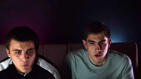 Two young guys are sitting on the couch in front of the TV and playing a game co Video stock 131196820