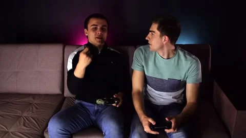 Two young guys are sitting on the couch in front of the TV and playing a game co Stock Footage 131196826