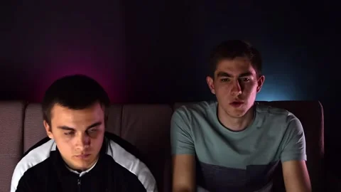 Two young guys are sitting on the couch in front of the TV and playing a game co Stock Footage 131196831