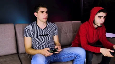 Two young guys are sitting on the couch in front of the TV and playing a game Stock Footage 134205131