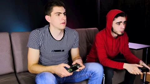 Two young guys are sitting on the couch in front of the TV and playing a game Stock Footage 134205133