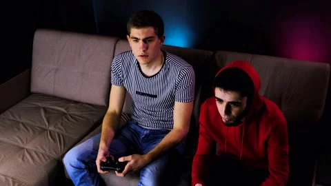 Two young guys are sitting on the couch in front of the TV and playing a game Stock Footage 134205163