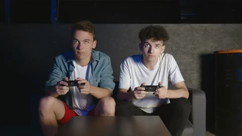 Two young guys are sitting on the couch in front of the TV and excited playing a Stock Footage 136330547