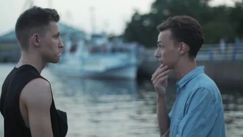 Two young guys talking near the water on the embankment in the evening, Slow Видео 113065997