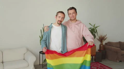 Two young handsome guys let up a lgbt flag, look at each other and smile Stock Footage 173798788