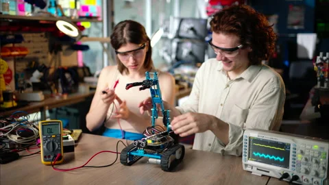 Two young happy engineers fixing a mechanical robot car in the workshop, using Stock Footage 247417749