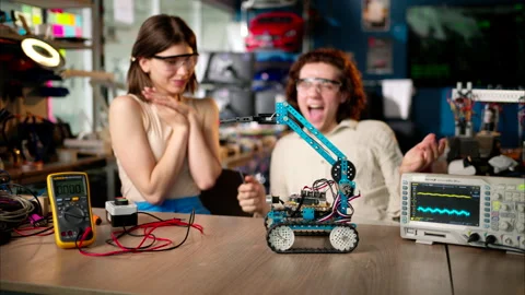 Two young happy engineers fixing a mechanical robot car in the workshop, using Stock Footage 247418077