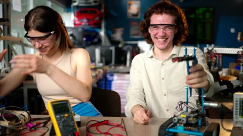 Two young happy engineers fixing a mechanical robot car in the workshop, using Stock Footage 247418254