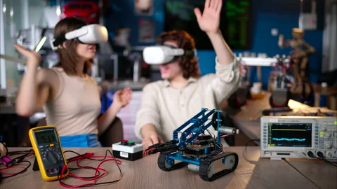 Two young happy engineers fixing a mechanical robot car in the workshop, using Stock Footage 247418766