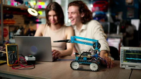Two young happy engineers fixing a mechanical robot car in the workshop, Stock Footage 247419272