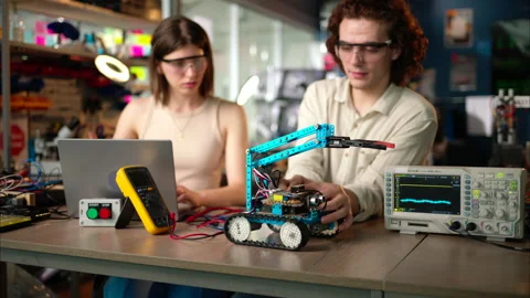 Two young happy engineers fixing a mechanical robot car in the workshop, Stock Footage 247419582